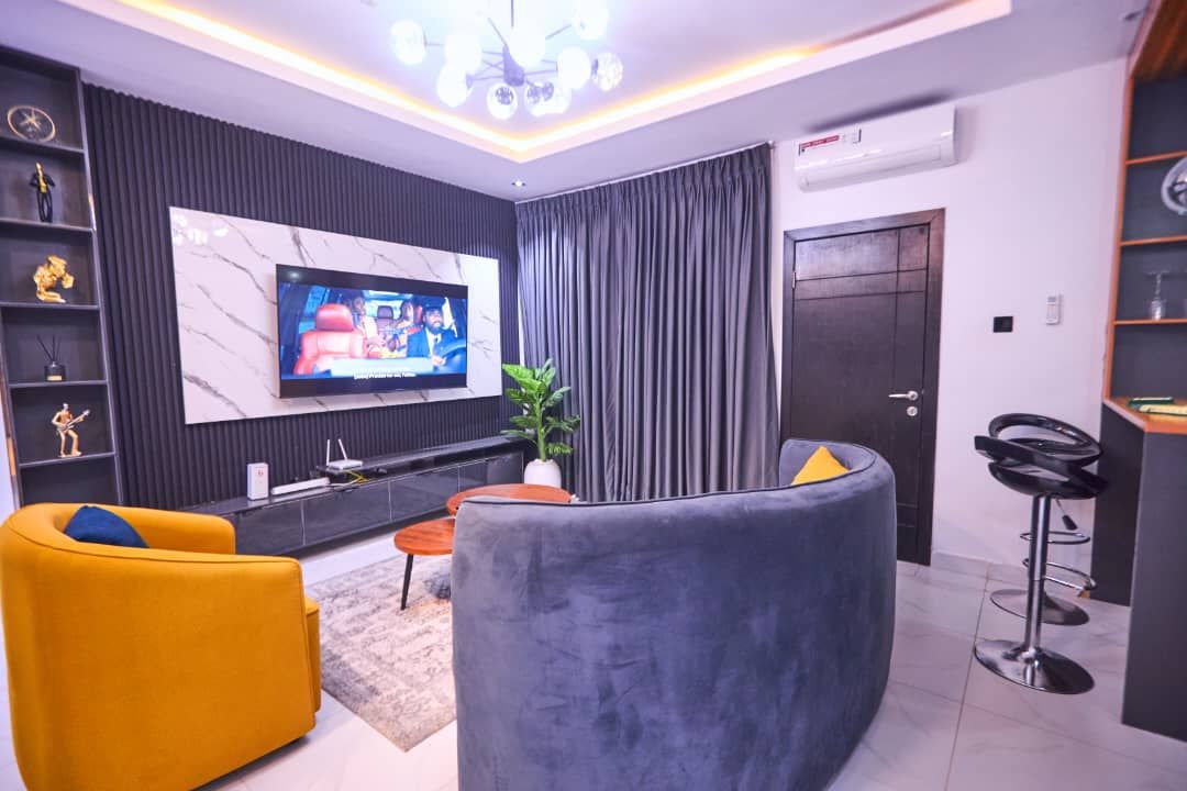 Una sala de estar moderna con un televisor de pantalla plana, un sofá, un sillón amarillo, una mesa de centro y una planta en maceta.