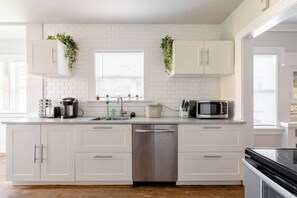 A modern kitchen with white cabinetry, a stainless steel dishwasher, a microwave, and a coffee maker. - A Block from Alberta St • 4BR • Sleeps 10 (Portland)