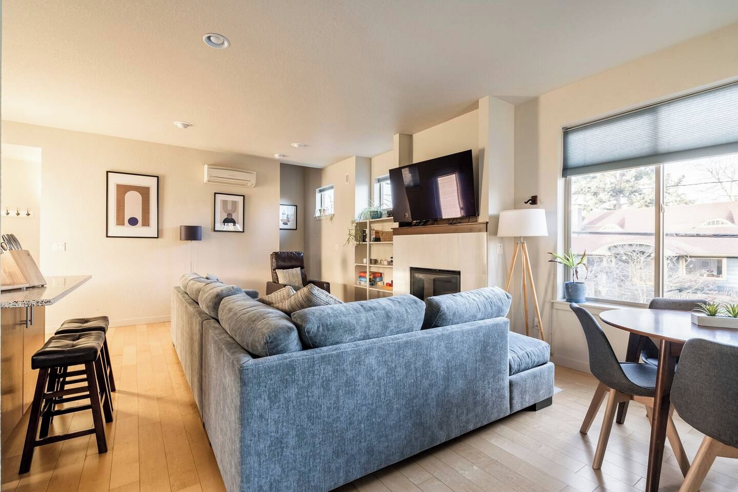 A modern living room with a sectional sofa, a flat-screen TV, a fireplace, and a dining area with a table and chairs.