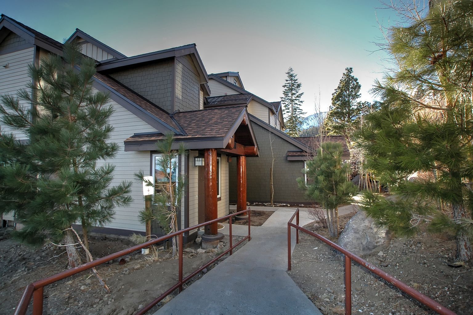 A residential property with a covered walkway leading to a house, surrounded by pine trees.