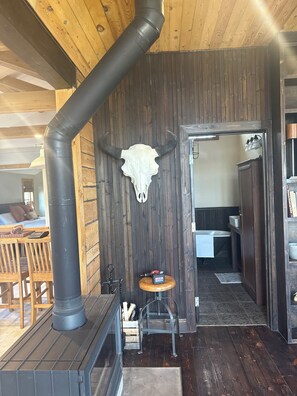 A rustic interior with a wooden ceiling, a black pipe, a wooden table with chairs, a small wooden stool, and a metal chair. - Remodeled 1885 Gallatin River Cabin Close to Big Sky and Bozeman (Bozeman)