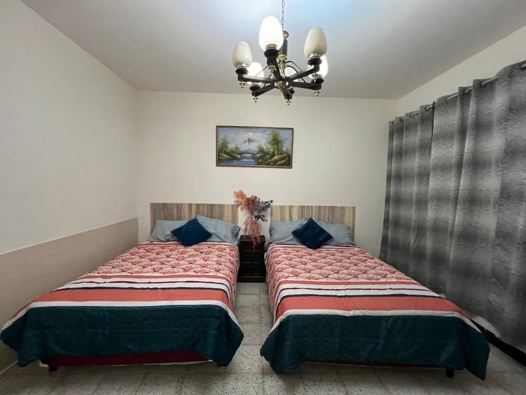 Una habitació amb dos llits, una làmpada penjolada, un quadre i una cortina.