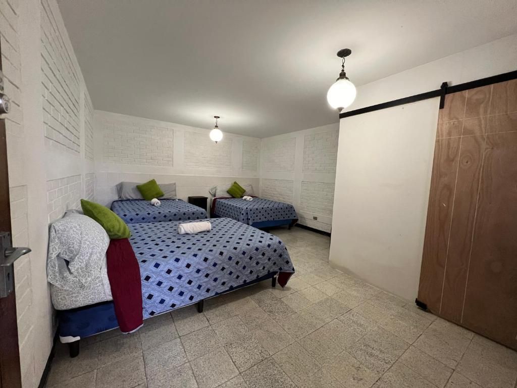 A room with two beds, each with a patterned bedspread, pillows, and a blanket. There are two wall-mounted light fixtures.