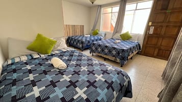 A room with two beds, each with patterned bedding, a wooden door, and a window with curtains.