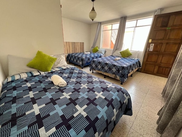 Una habitación con dos camas, cada una con ropa de cama estampada, una puerta de madera y una ventana con cortinas.