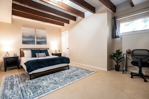 Un dormitorio con cama, mesitas de noche, un escritorio y una ventana.