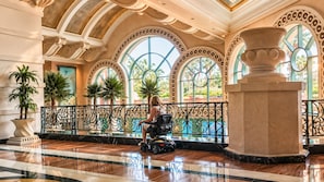 Un hall amplio con piso de mármol, ventanas grandes con arcos decorativos y plantas en macetas.