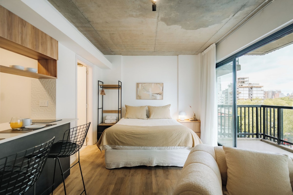 Een moderne slaapkamer met een bed, een bureau en een balkon met uitzicht op de stad.