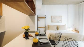Een moderne hotelkamer met een zithoek, een bed met wit dekbedovertrek, een zwarte draadstoel en een wandrek.