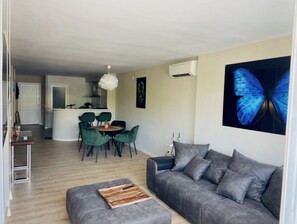 Un saló modern amb un sofà gris, una taula de centre de fusta i una zona de menjador amb cadires verdes.