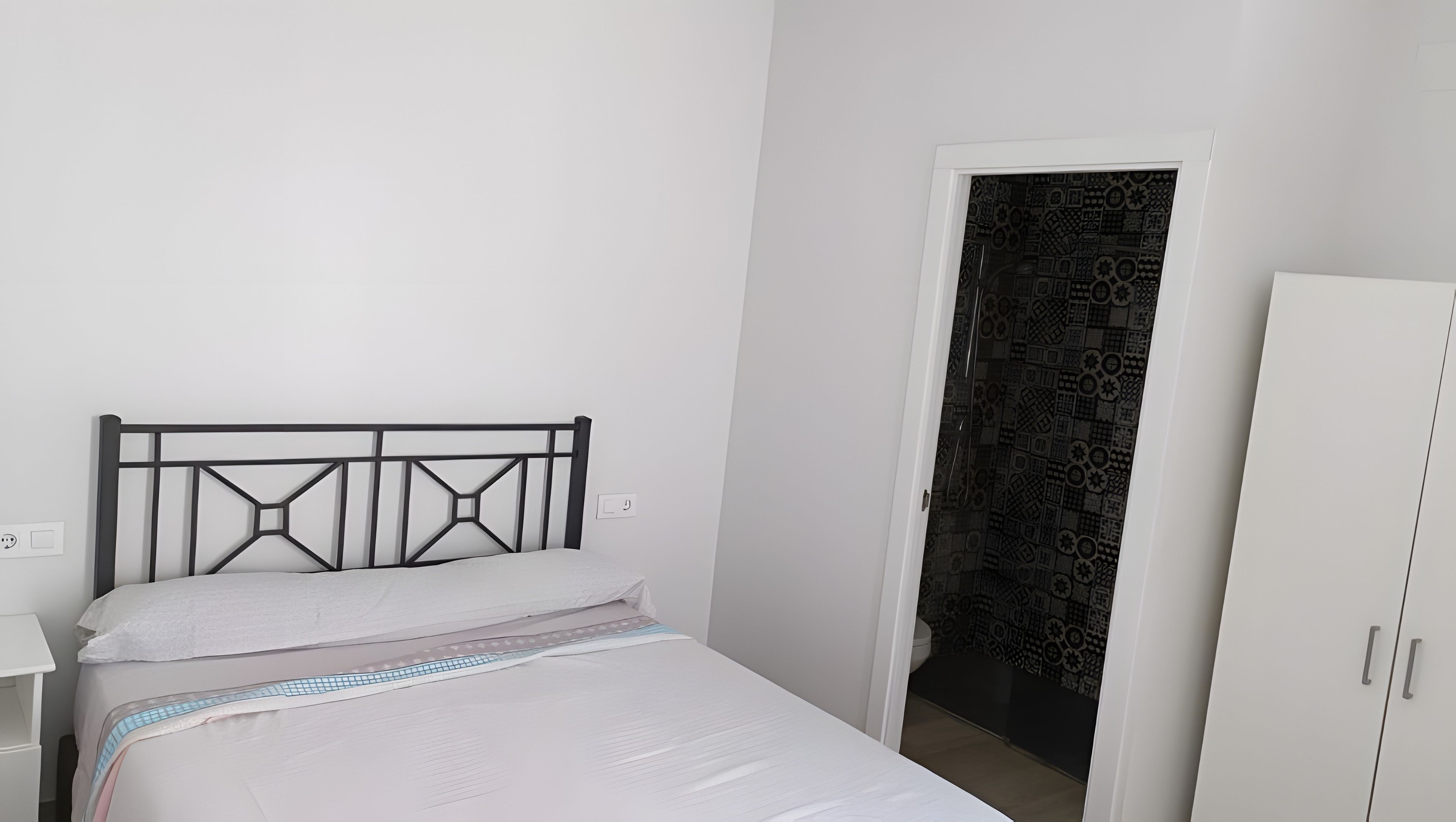 Een slaapkamer met een bed, een kledingkast en een deur naar een betegelde badkamer.