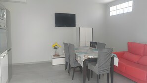 Habitació moderna amb taula de dinar, cadires, un sofà vermell, televisió de pantalla plana i un petit vas decoratiu amb flors.