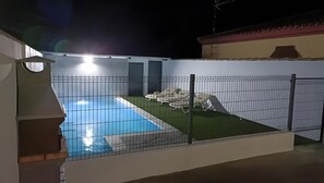 Una piscina amb una zona tancada per una tanca, gandules i un edifici al fons.