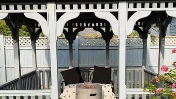 A covered outdoor seating area with a table and chairs, surrounded by a wooden fence and potted plants.