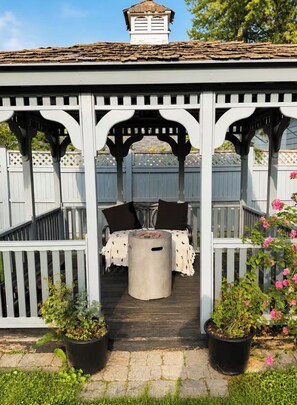 Un espacio de estar al aire libre cubierto con una mesa y sillas, rodeado por una valla de madera y plantas en macetas.