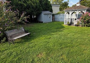 Een achtertuin met een houten bankje, een tuinhuisje en een prieeltje.
