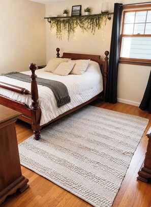 Een slaapkamer met een houten bed, een wit vloerkleed en een plank met planten.