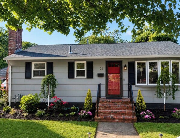 A single-story house with a red front door, white siding, and a brick chimney.