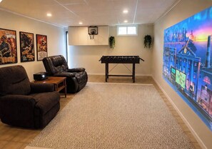 A room with a foosball table, a large wall mural, and a basketball hoop.