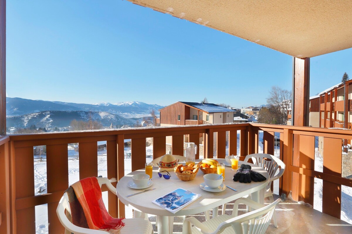 Varanda com mesa posta para o café da manhã, com vista para uma paisagem montanhosa coberta de neve.