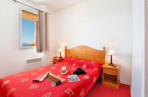 Quarto de hotel com cama de madeira, duas mesas de cabeceira com luminárias, janela com cortinas e radiador.