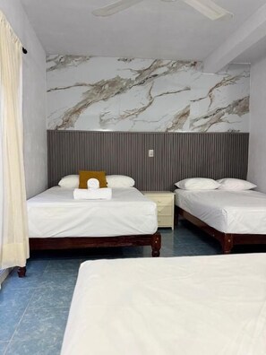 Une chambre d’hôtel avec deux lits, un mur décoré d’un motif imitant le marbre et un ventilateur de plafond.