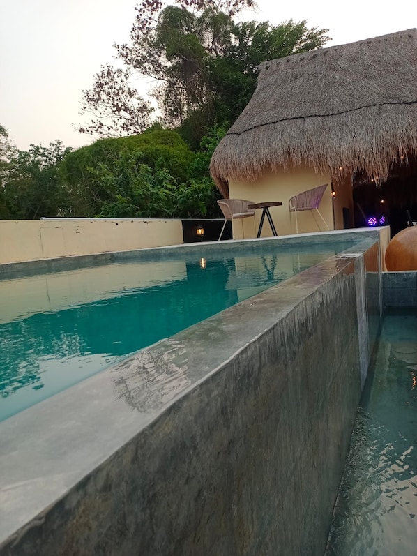 Une piscine avec une structure couverte d’un toit de chaume en arrière-plan.