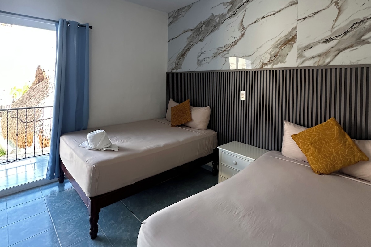 Une chambre d’hôtel avec deux lits, un ventilateur de plafond, une grande fenêtre avec des rideaux et un mur en marbre.