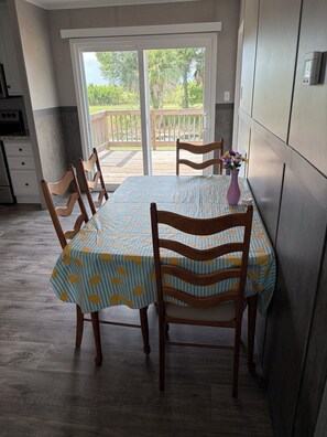 A dining area with a table set for four, wooden chairs, a vase with flowers, and a view of the outdoors through a sliding glass door. - The Canal House on the canal with stunning sunsets. (Okeechobee)