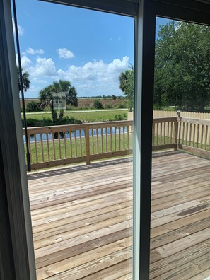 A wooden deck with a view of a grassy field and trees. - The Canal House on the canal with stunning sunsets. (Okeechobee)