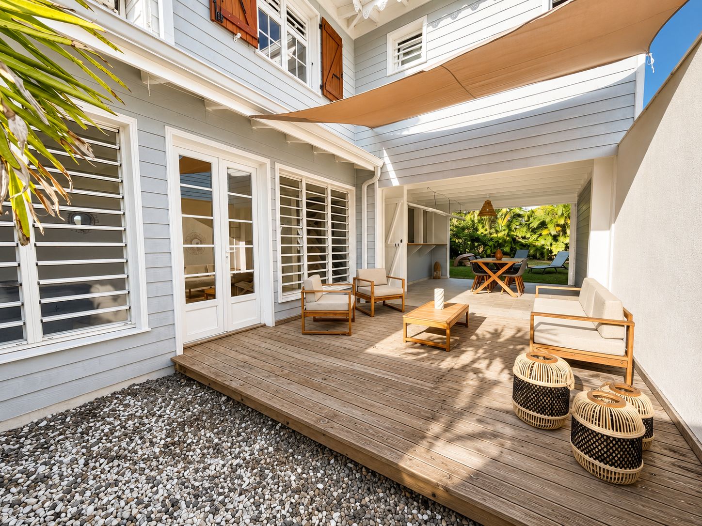 A covered patio with outdoor furniture, a wooden deck, and a view of a lush garden.