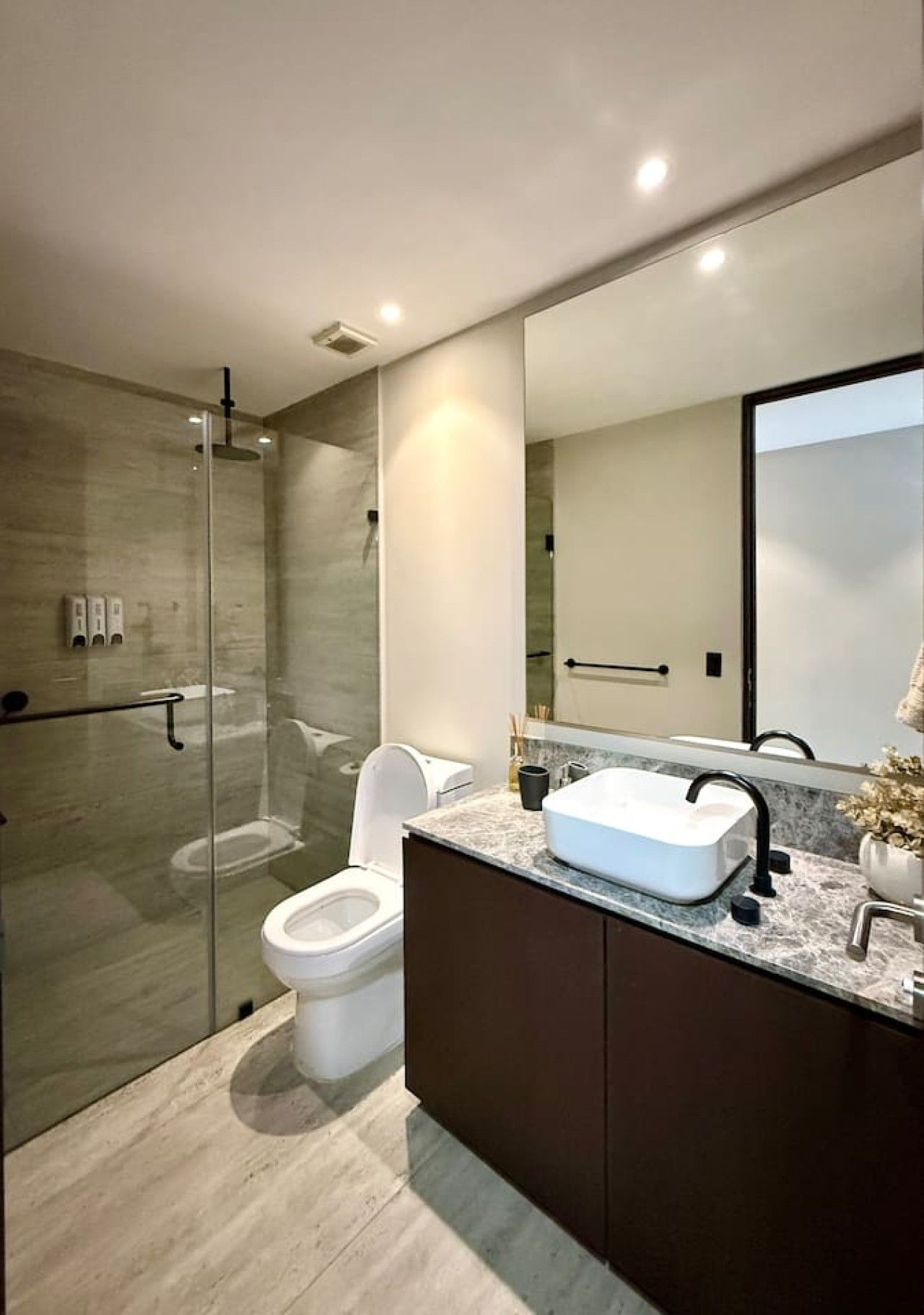 Et moderne badeværelse med et brusebad bag glasvæg, et hvidt toilet og en marmorvaskebordplade med vask.
