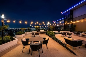 An outdoor seating area with tables and chairs, string lights, and a city view at night. - CUR-CUMA | Boutique 2BR | Americana (Guadalajara)
