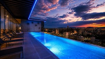 An infinity pool with a cityscape view, lounge chairs, and a modern building structure.