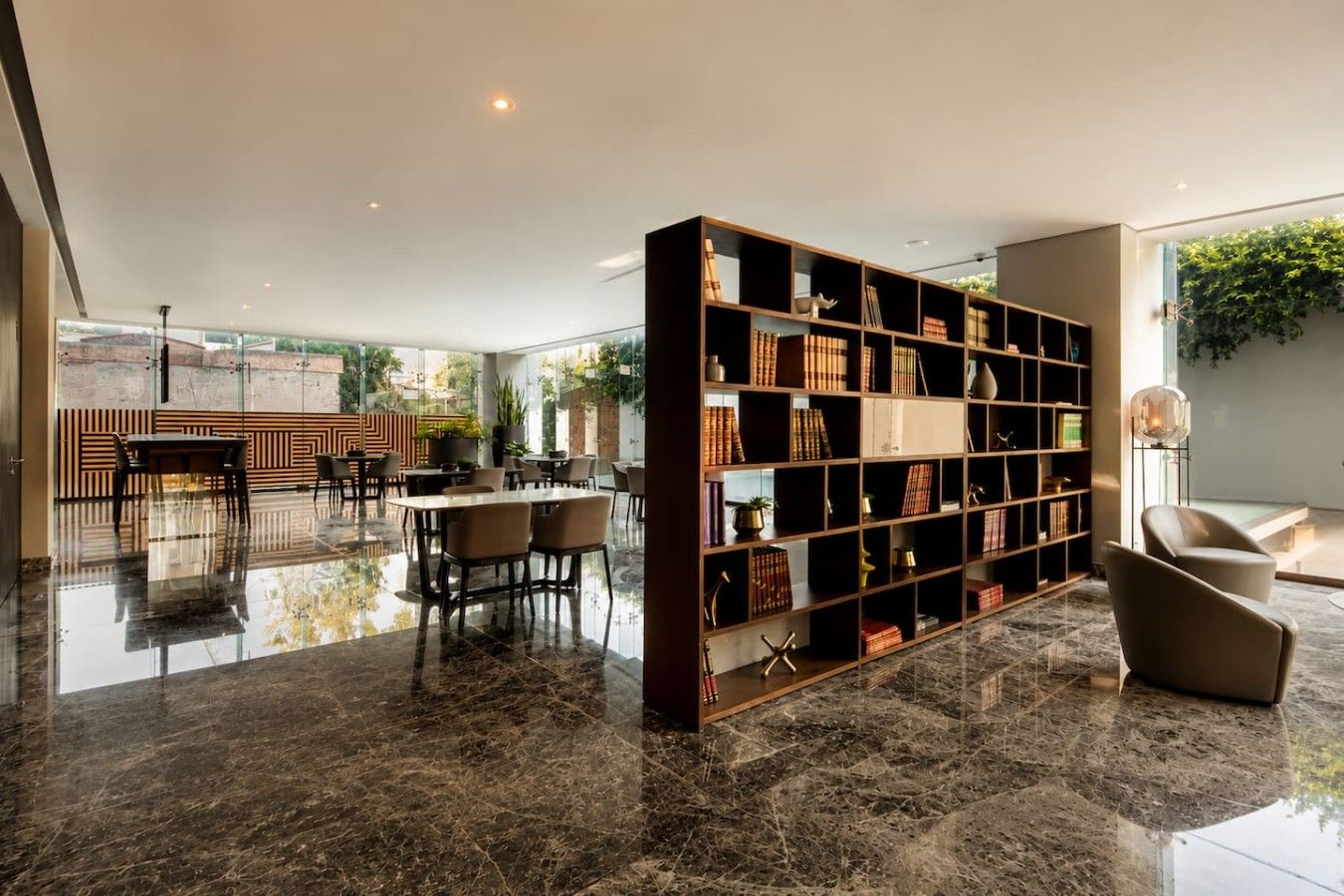 A modern living room with a marble floor, a large bookshelf, and a dining area with chairs and a table.