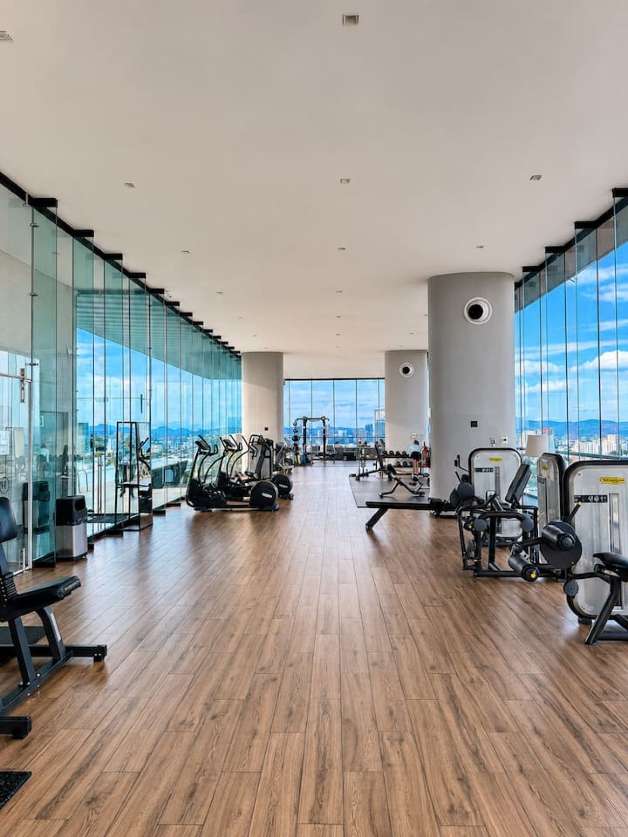 A spacious gym with cardio machines, free weights, and a large window offering a city view.