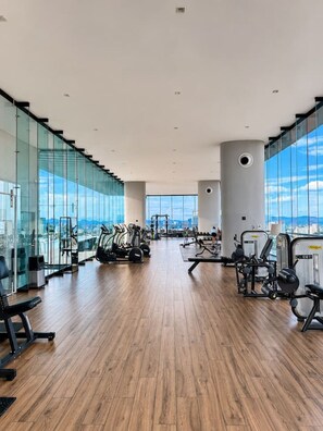 A spacious gym with cardio machines, free weights, and a large window offering a city view. - AUREA | Luxury 2BR Rooftop Pool | Americana (Guadalajara)