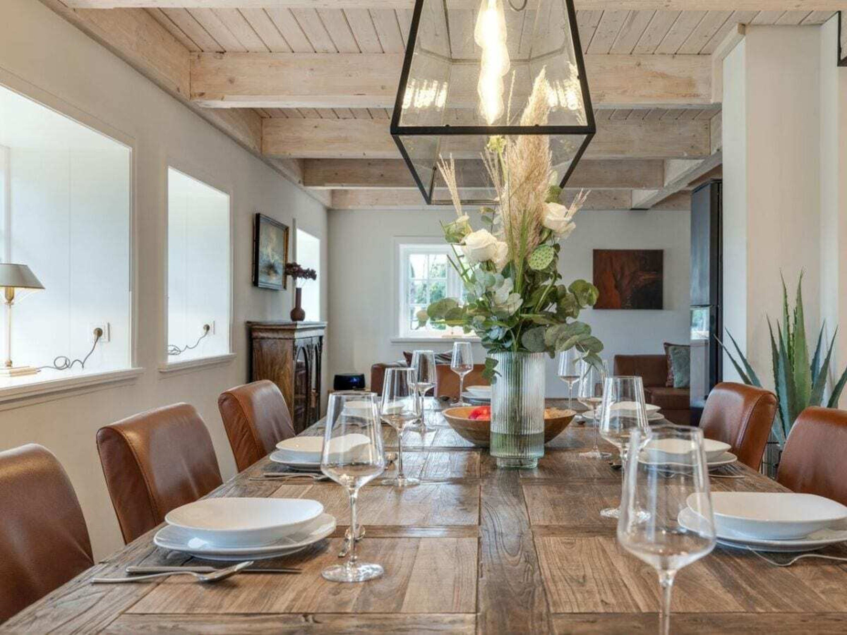 Uma sala de jantar com mesa de madeira posta para seis pessoas, rodeada por cadeiras de couro.
