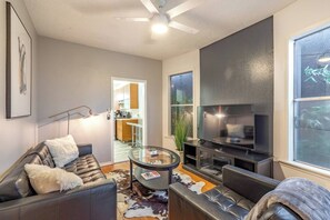 Ein modernes Wohnzimmer mit einer Ledersofa, einem Glastisch, einem Flachbildfernseher und einem Deckenventilator.