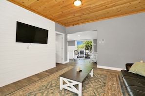 Una sala de estar moderna con un televisor de pantalla plana montado en la pared, techo de madera y alfombra estampada.