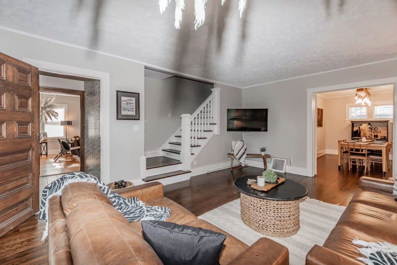 Een moderne woonkamer met een bruine leren bank, een ronde salontafel en een trap naar een hoger niveau.