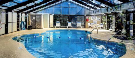 Una piscina interior con techo de cristal, sillas de piscina y puesto de socorrista.