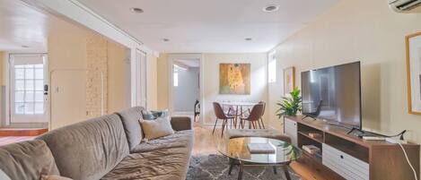 A living room with a sofa, a glass coffee table, a TV, and a dining area with chairs.