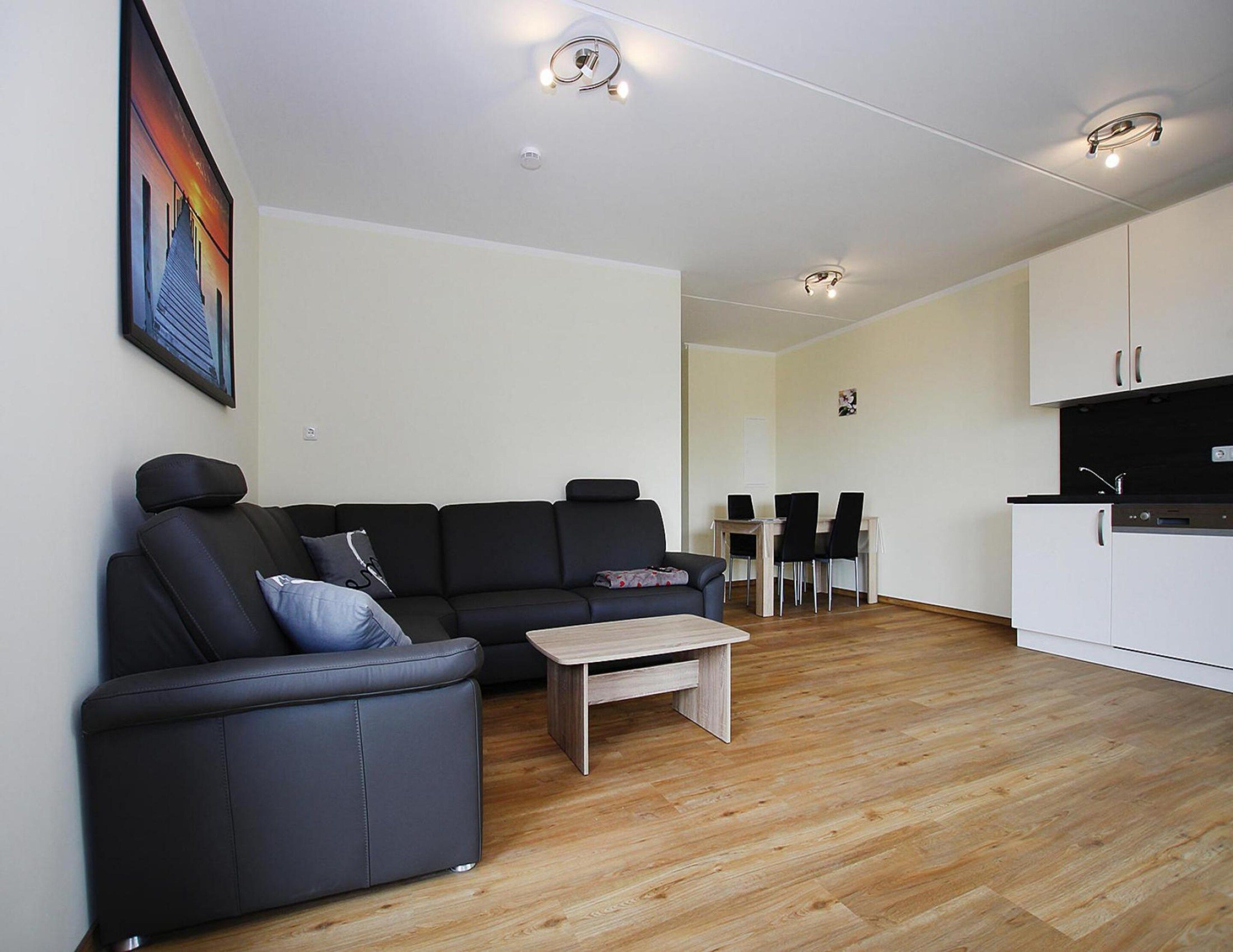 A modern living room with a black sofa, a wooden coffee table, and a dining area with a white table and chairs.