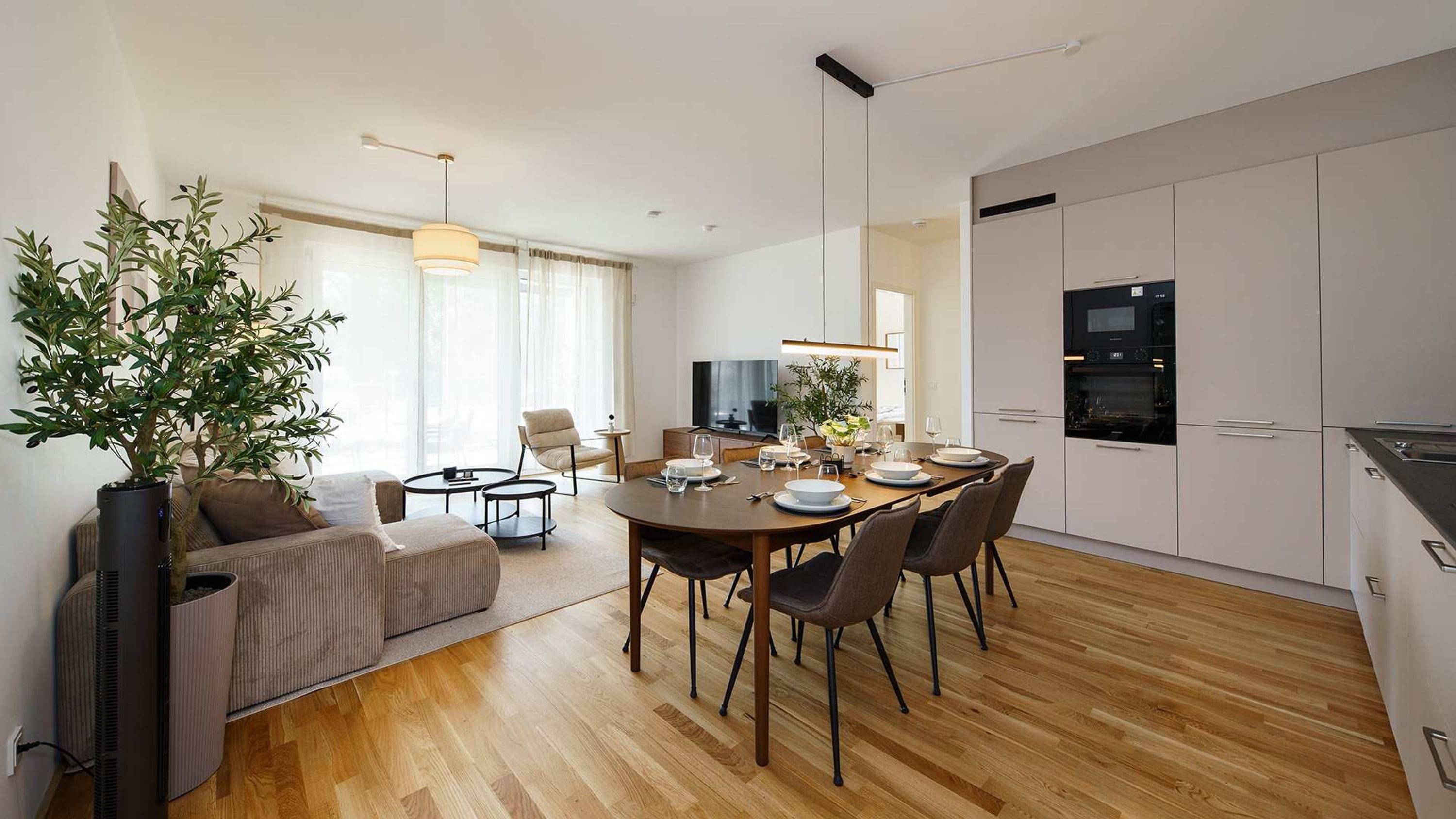 Een moderne keuken met een eethoek, houten vloeren en een grote potplant.