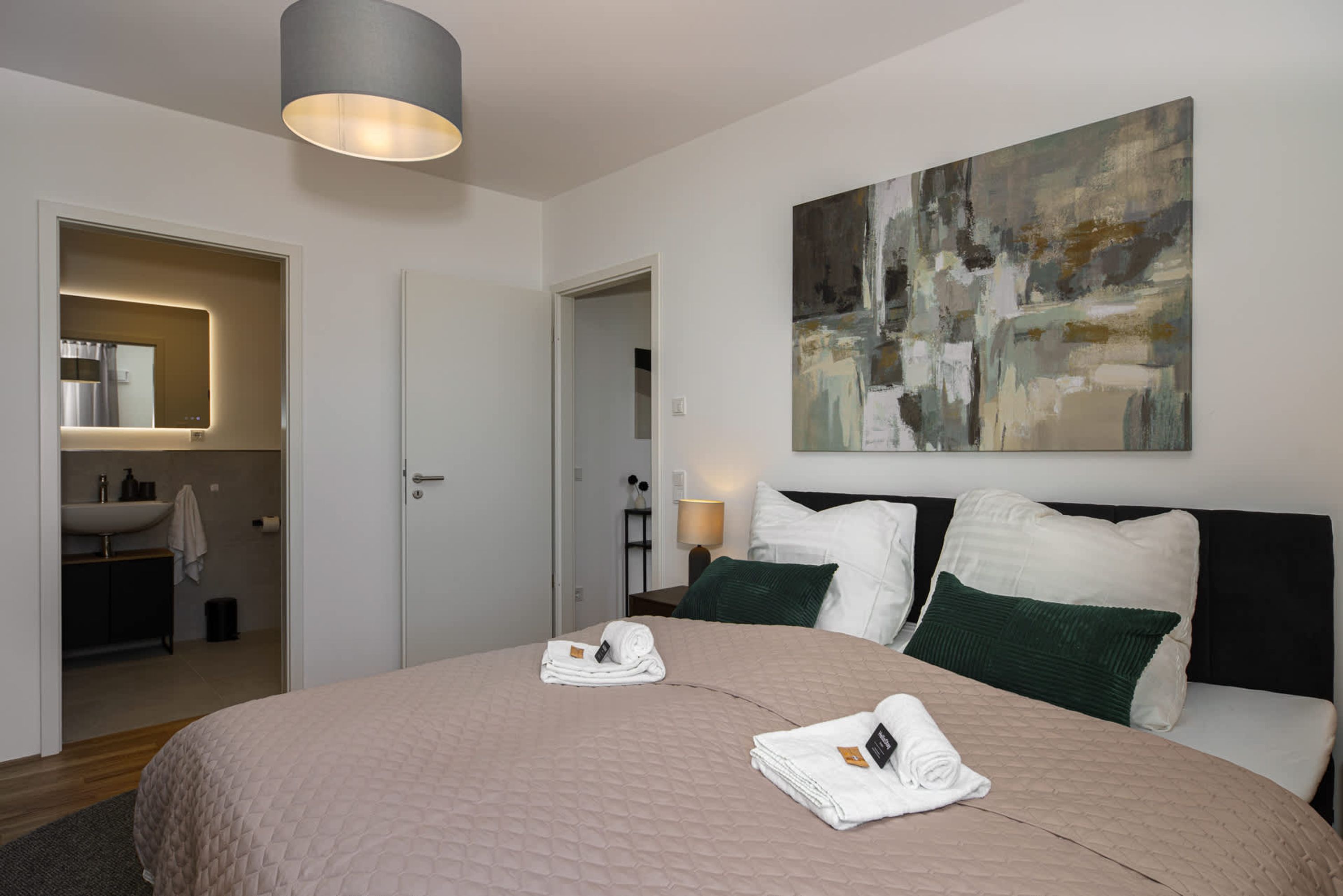 Ein modernes Hotelzimmer mit einem großen Bett, einem Gemälde an der Wand und einem durchgegangenen Tür erkennbaren Badezimmer.