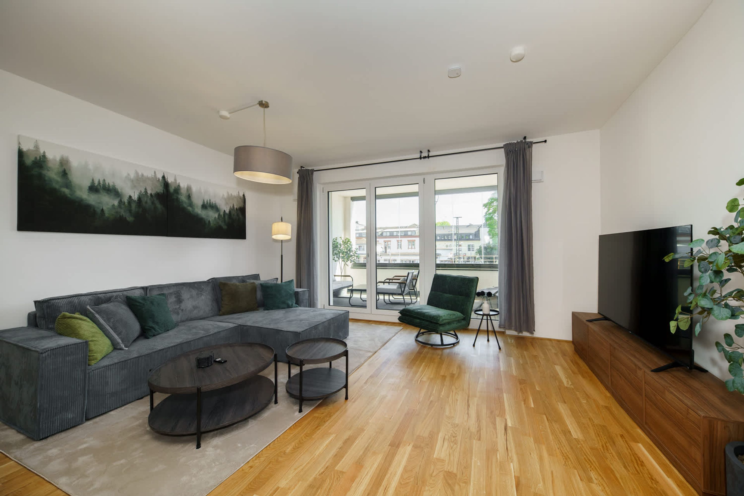 A modern living room with a sectional sofa, a coffee table, a TV, and a large window with a view of buildings.