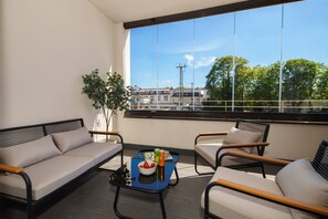 A balcony with a sofa, chairs, a table with a bowl of fruit and drinks, and a view of buildings and trees. - Luxury 4-room Apt in Boutique-style I Prime Location I Family-friendly I Balcony I Kitchen I Netflix I Free Parking I 110 m2 (Eltville am Rhein)