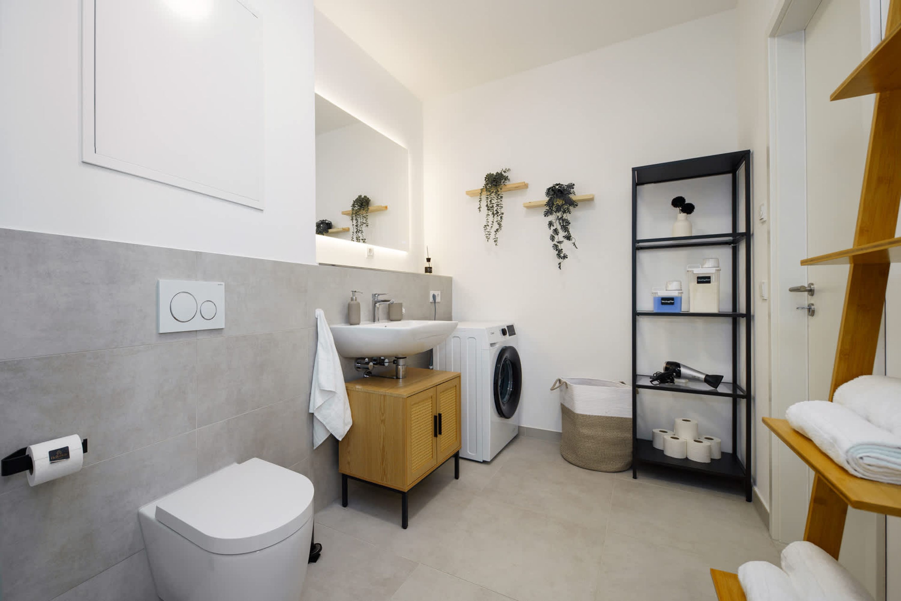 A modern bathroom with a toilet, sink, washing machine, and shelves with toiletries.