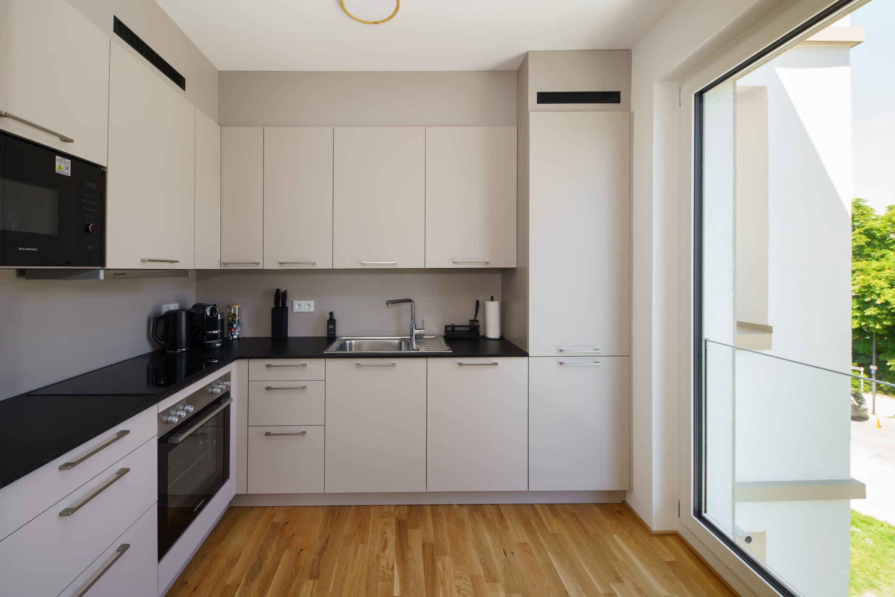 Une cuisine moderne avec des armoires blanches, un plan de travail noir et un plancher en bois.